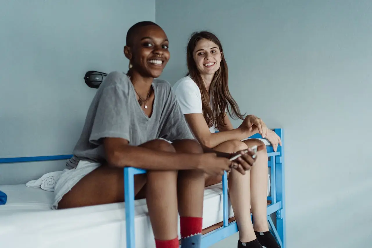Two women sitting on a bunk bed, smiling and enjoying their time indoors, capturing a moment of relaxation.