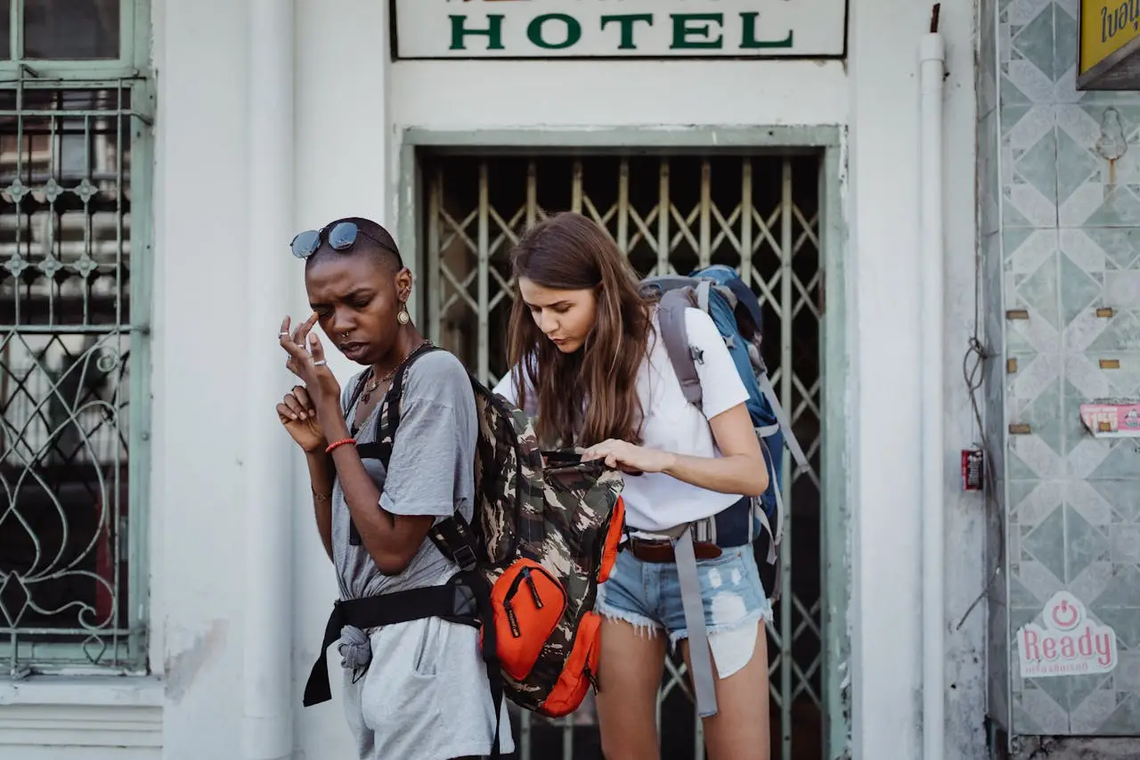 Two young female backpackers checking their belongings outside a hotel entrance.