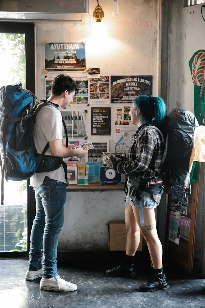 A young couple with backpacks examining travel brochures indoors, planning their next urban adventure.